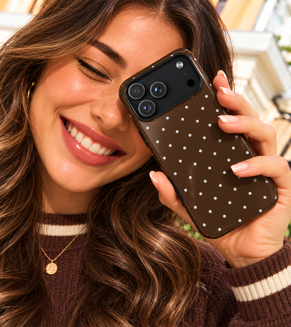 Lachende vrouw houdt een bruin telefoonhoesje met witte stippen bij haar gezicht
